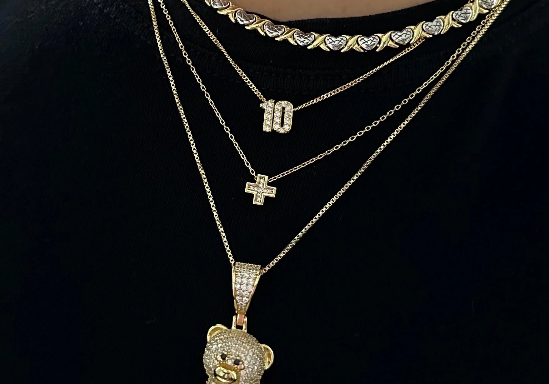 Baby Cross Necklace layered with a number necklace and iced teddy necklace on a black tee