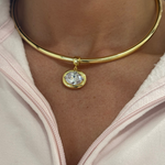 Model wearing a clear birthstone pendant on a gold cuff necklace
