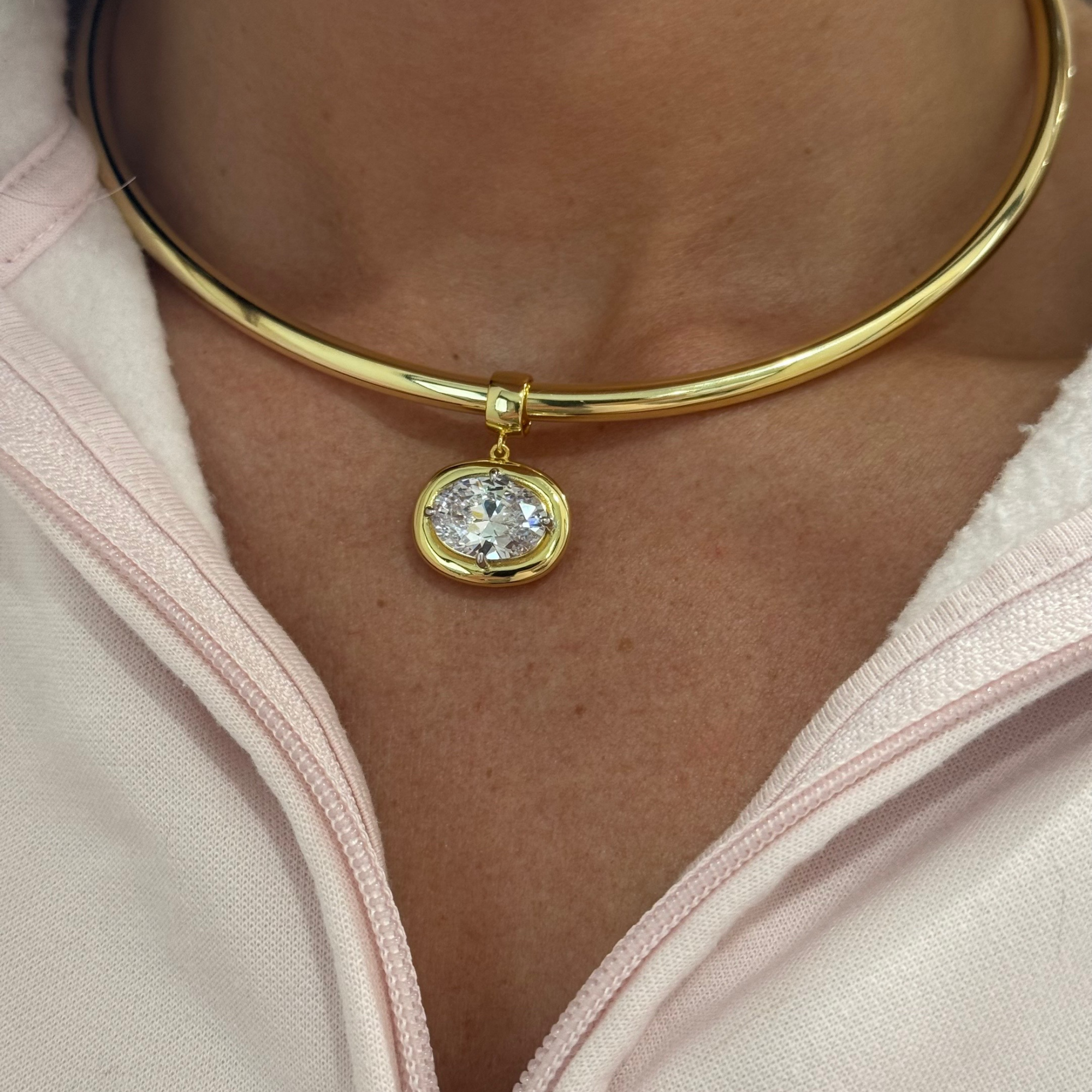 Model wearing a clear birthstone pendant on a gold cuff necklace