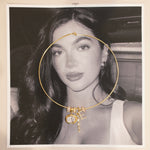 Gold cuff necklace with birthstone and charm pendants on a black and white photo