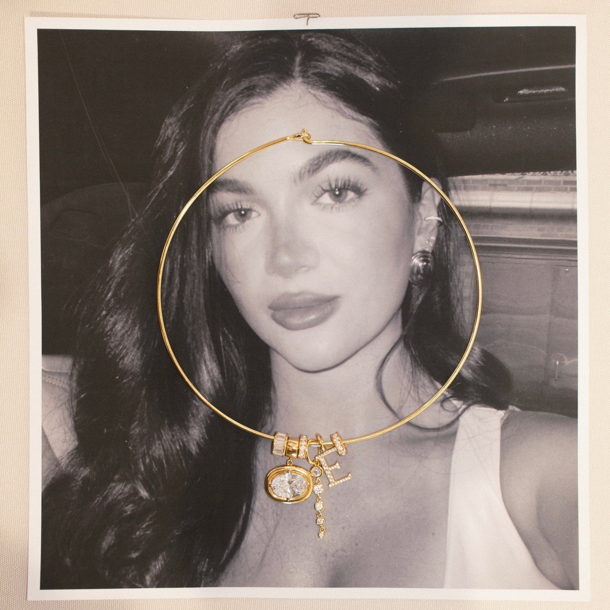 Gold cuff necklace with birthstone and charm pendants on a black and white photo