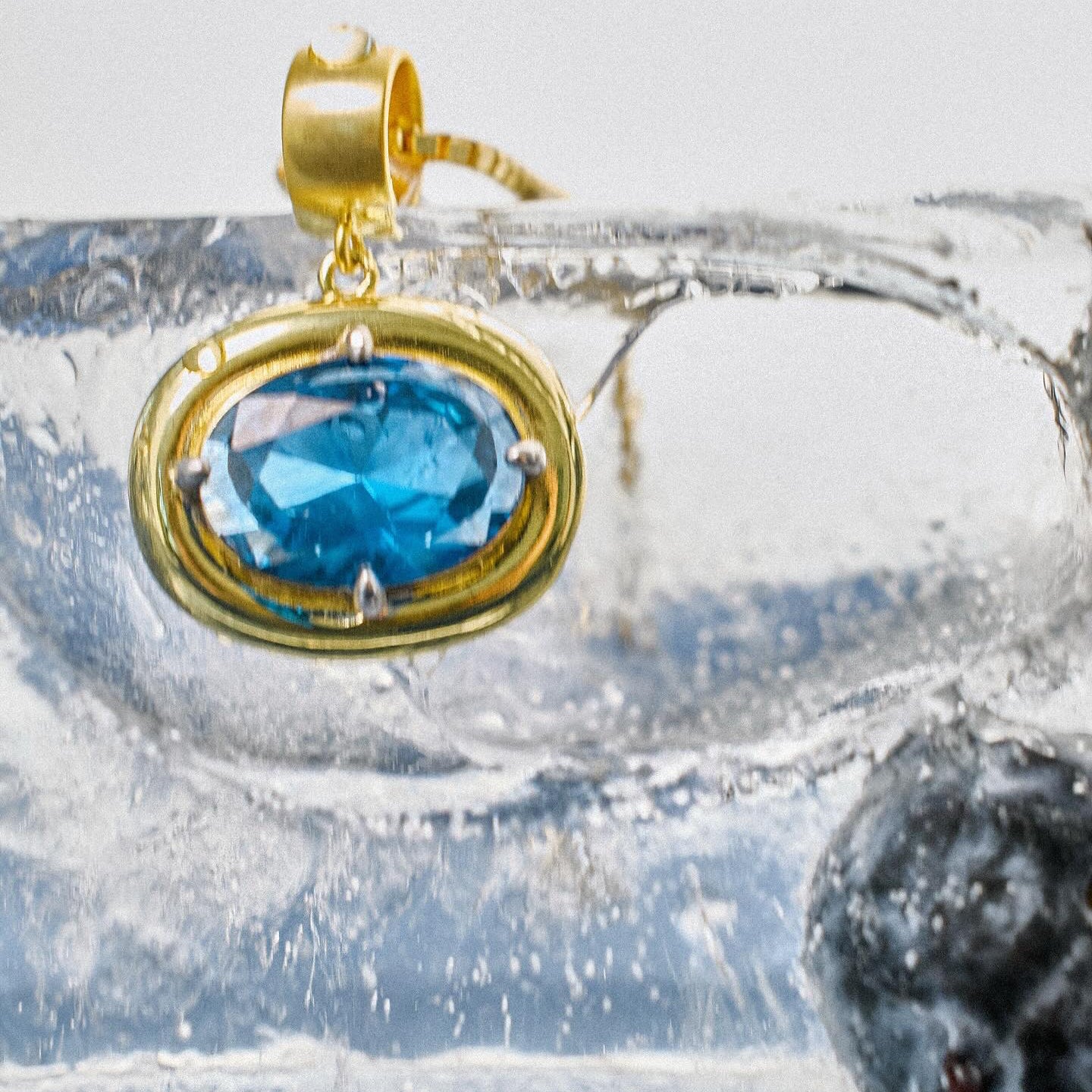 Close-up of a blue birthstone pendant in a gold bezel resting on ice