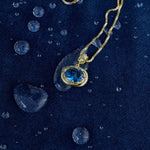 Blue birthstone pendant on a gold chain on denim with water drops