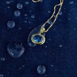 Blue birthstone pendant on a gold chain on denim with water drops