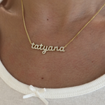 Model wearing the gold CZ Baby Script Nameplate in tatyana with a white top