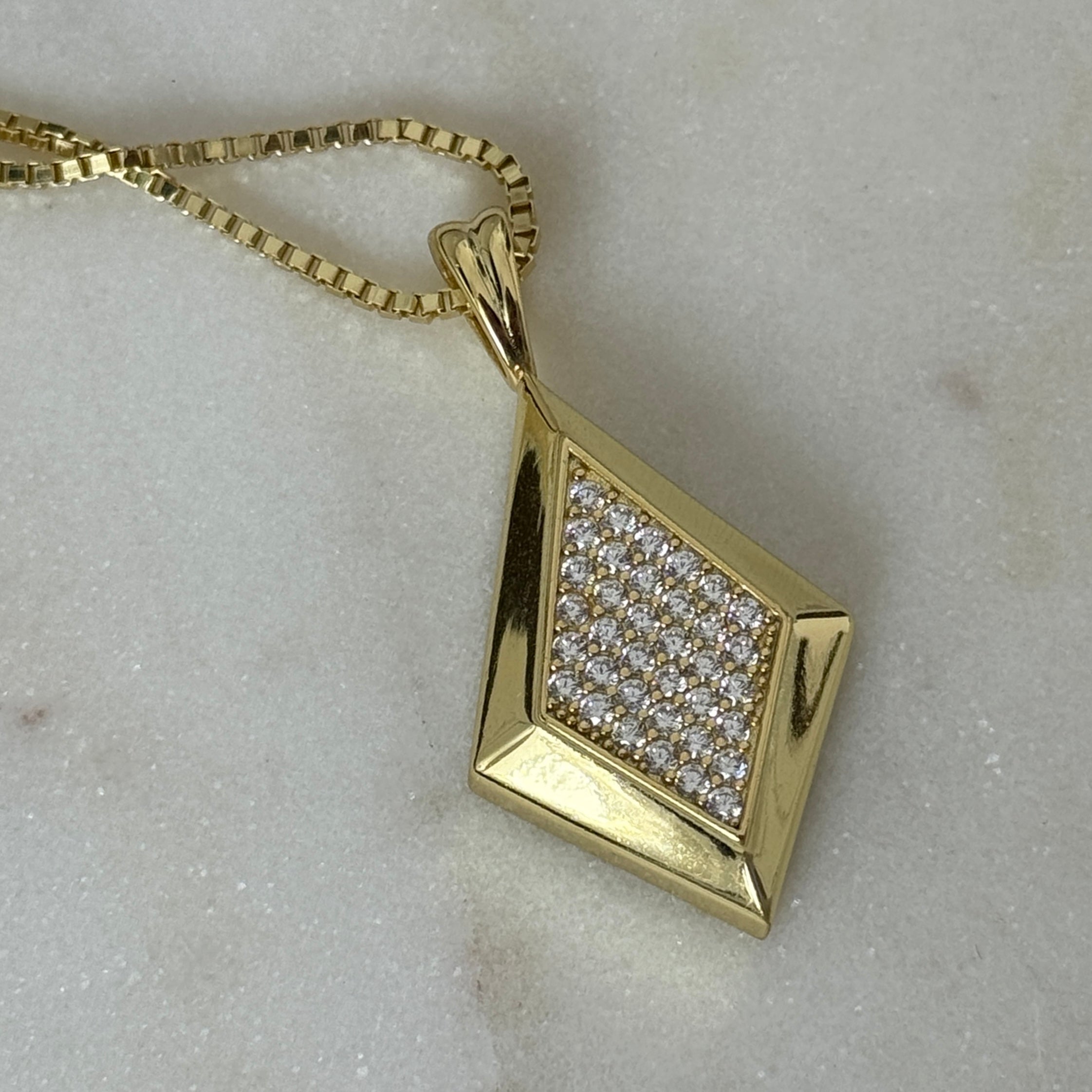 Close-up of the gold CZ Taylor pendant on a box chain on marble