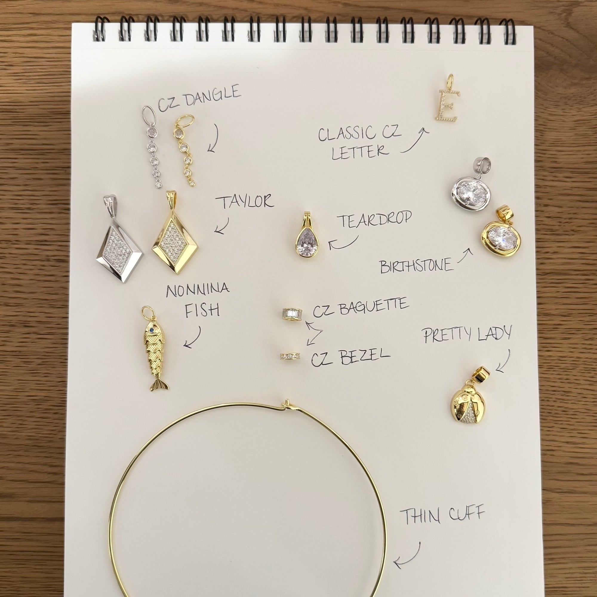 Sketchbook of EP Jewels cuff charms labeled by name with a thin gold cuff