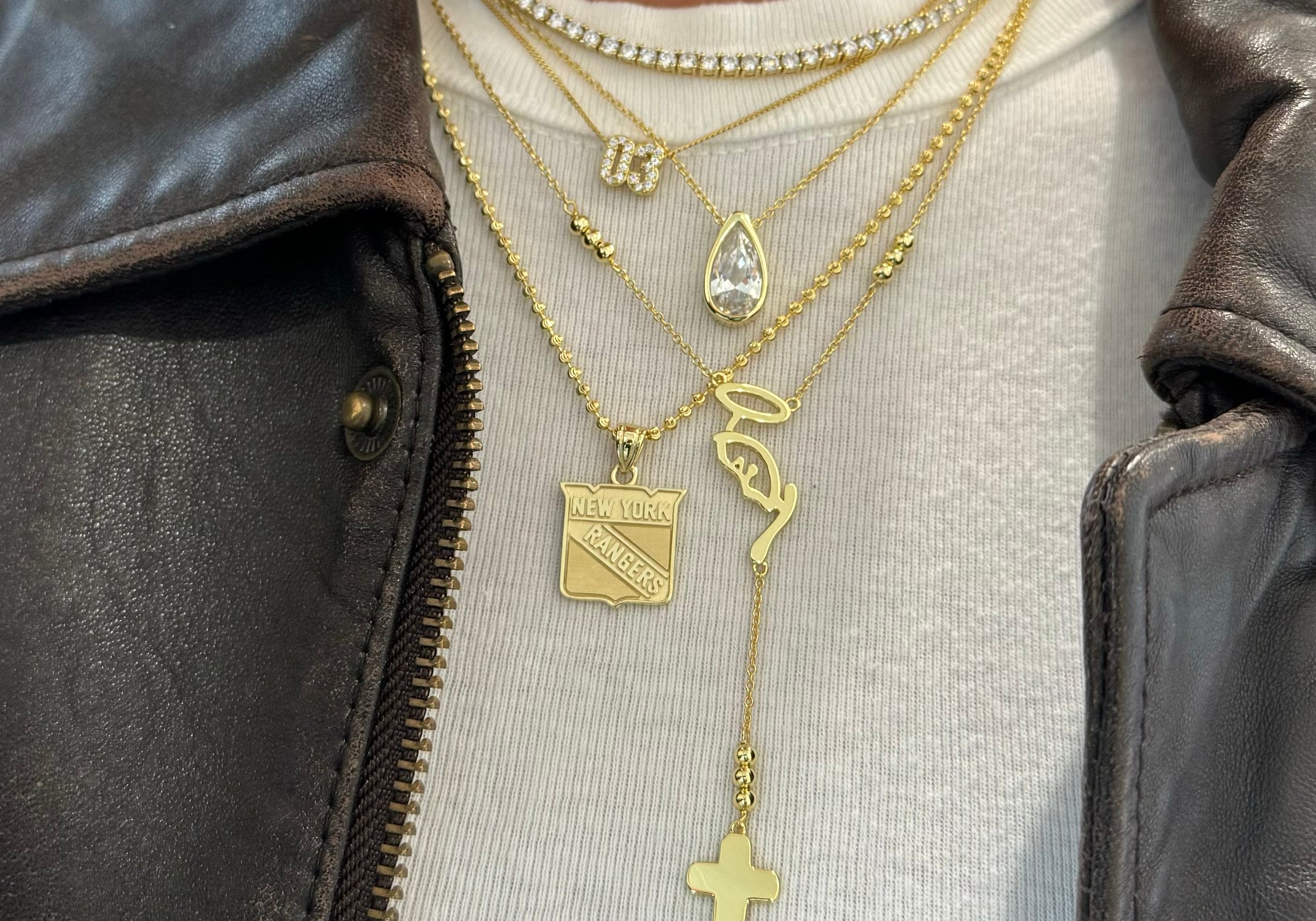 CZ Teardrop Necklace layered with gold charm necklaces over a white tee and leather jacket