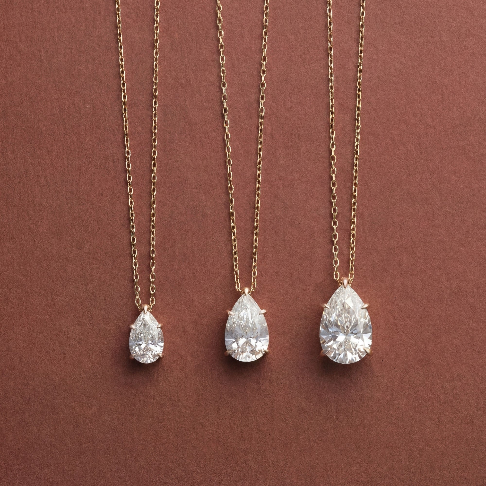 Three Classic Pear Diamond Necklaces in 0.5, 1 and 2 ctw on a brown background, 14K solid gold