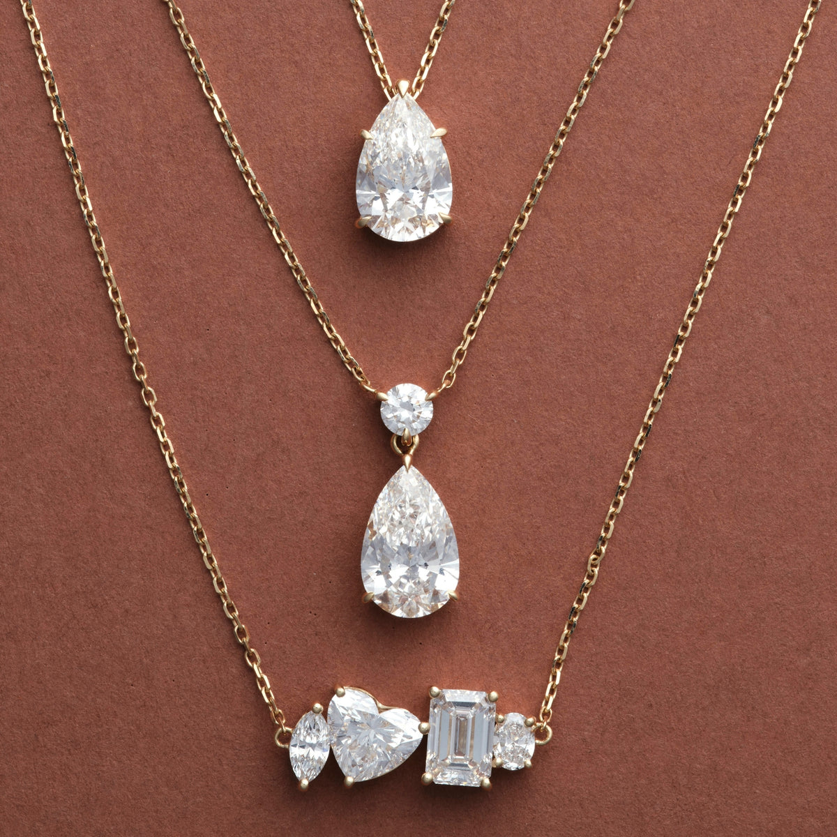 Classic Pear, Pear Dangle and Multi Shape Diamond Necklaces in 14K solid gold on a brown background