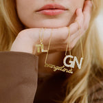 Hand holding script and initial nameplate necklaces