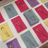EP Jewels gold hair pins displayed on hot pink, butter yellow, lavender and baby blue pouches