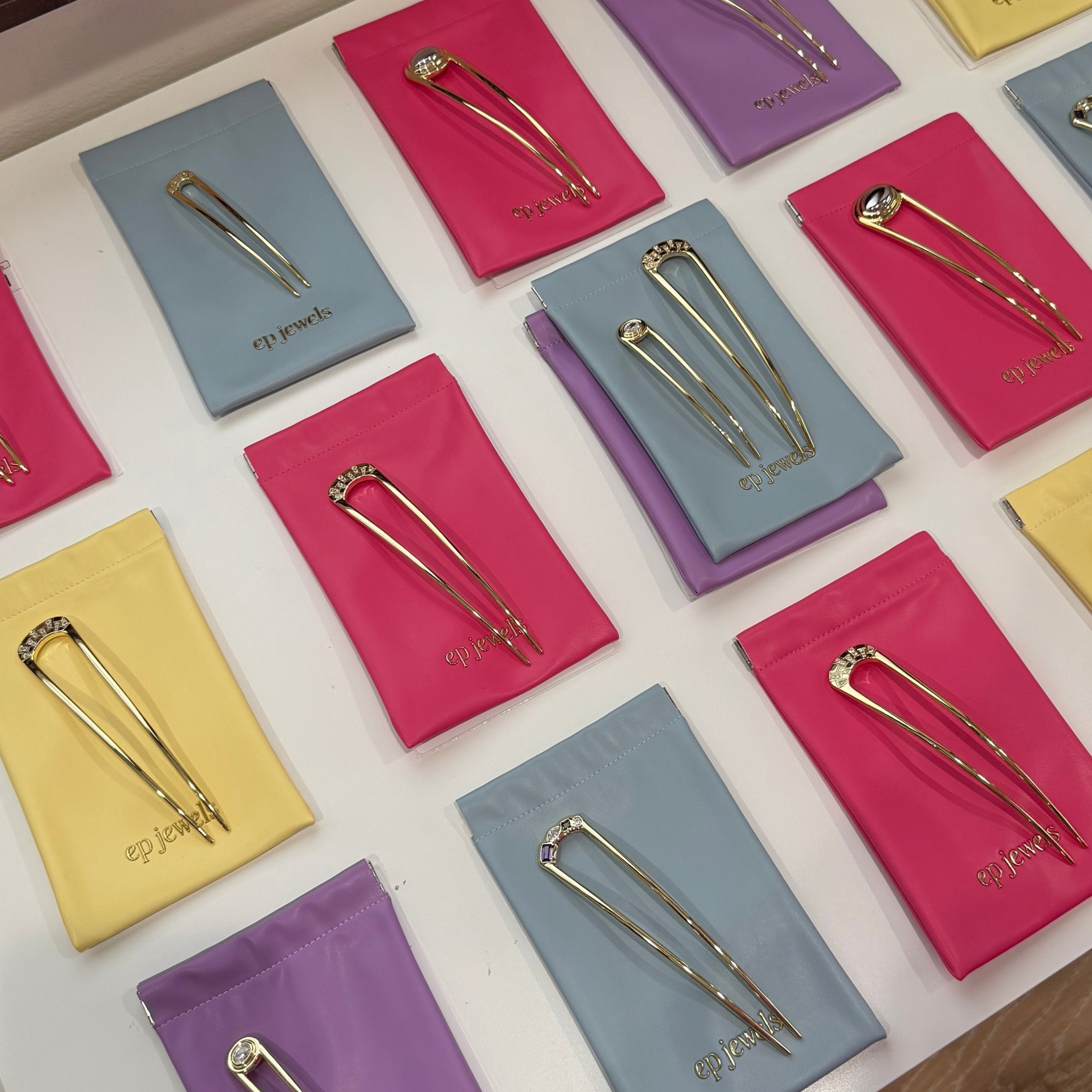 EP Jewels gold hair pins displayed on hot pink, butter yellow, lavender and baby blue pouches