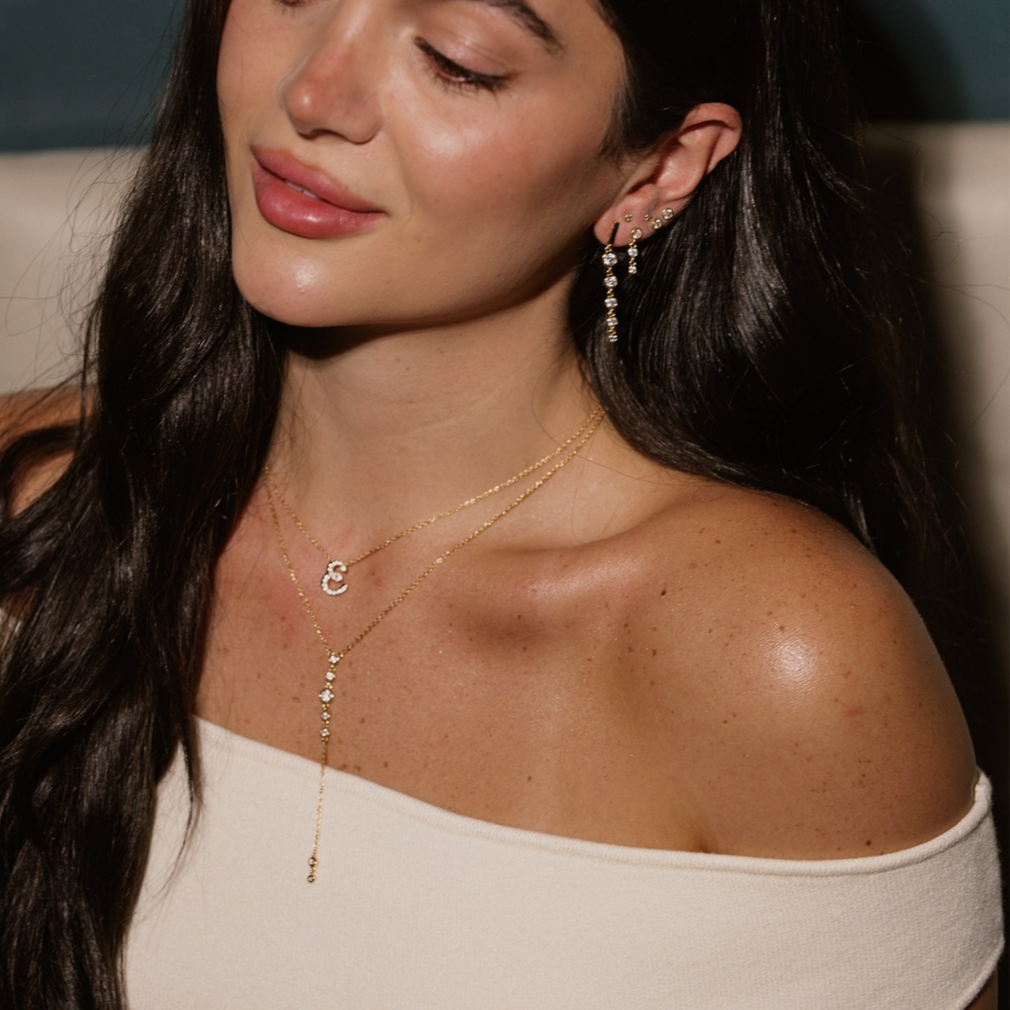 Model wearing a dainty gold iced script initial necklace with an off-shoulder top