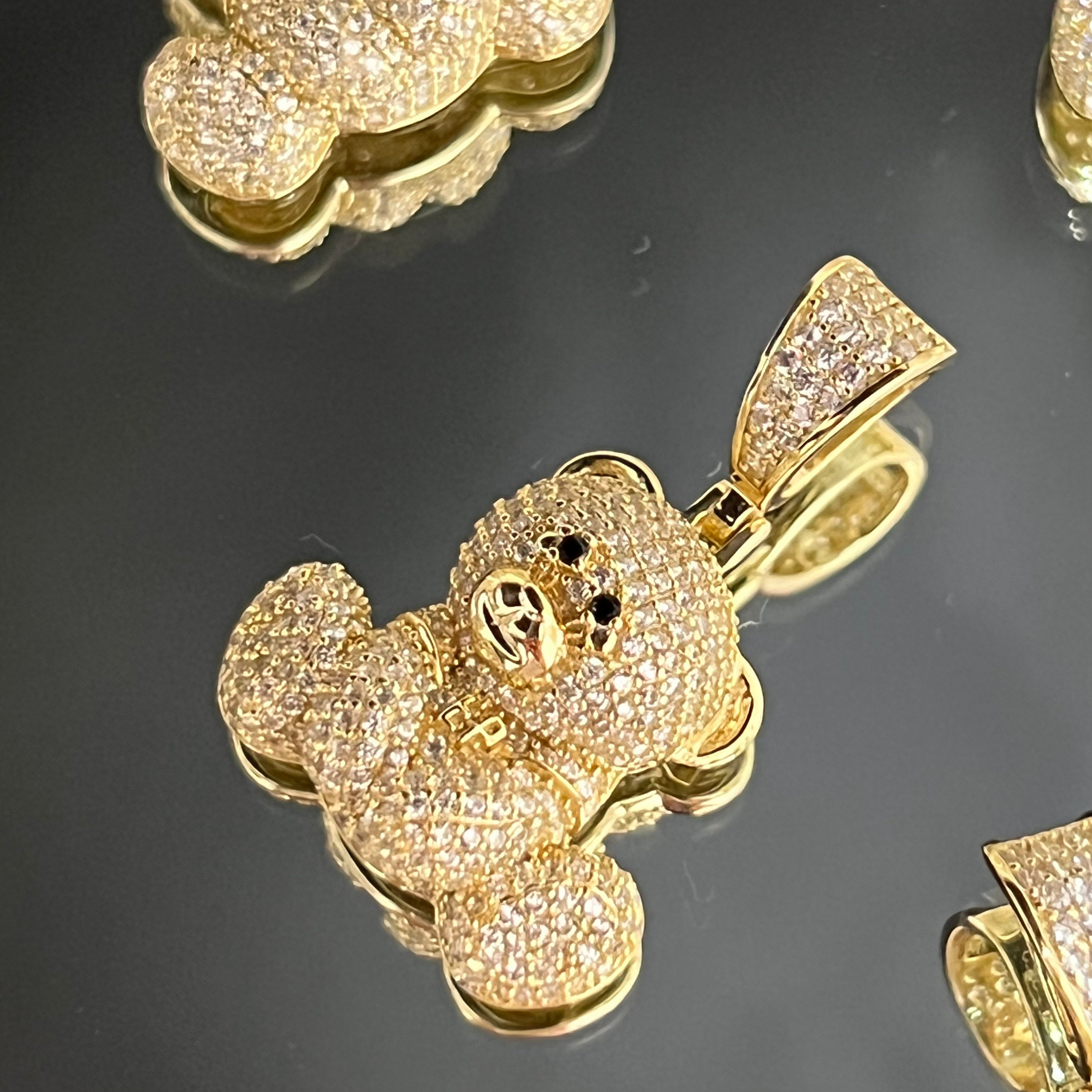 Close-up of gold CZ-iced EP Teddy pendants on a black surface