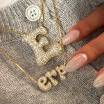 Iced Jumbo Initials Necklace layered with an iced letter E necklace on a grey sweater