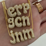 Hand holding three gold Iced Jumbo Initials Necklaces in erp, gcn and jnm