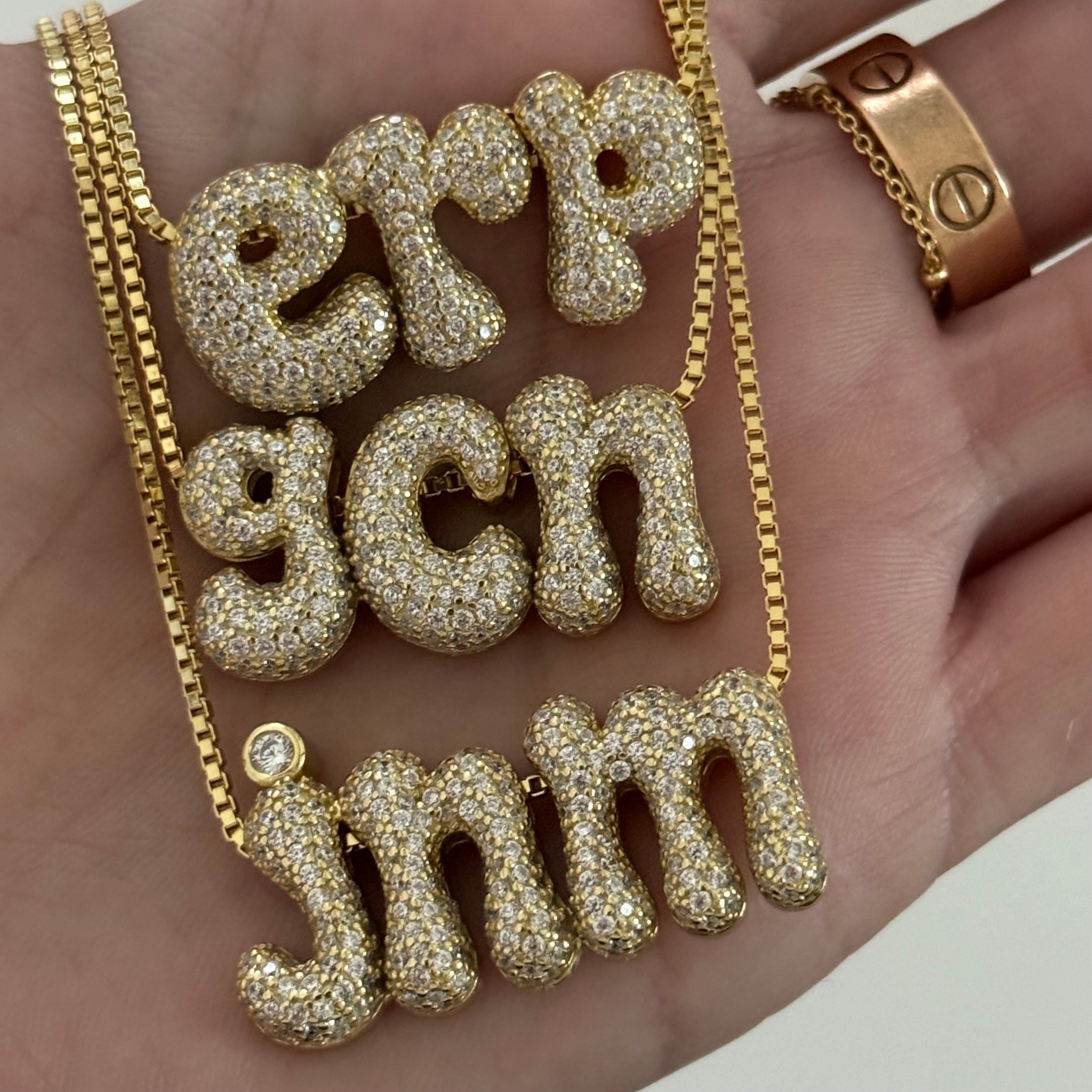 Hand holding three gold Iced Jumbo Initials Necklaces in erp, gcn and jnm