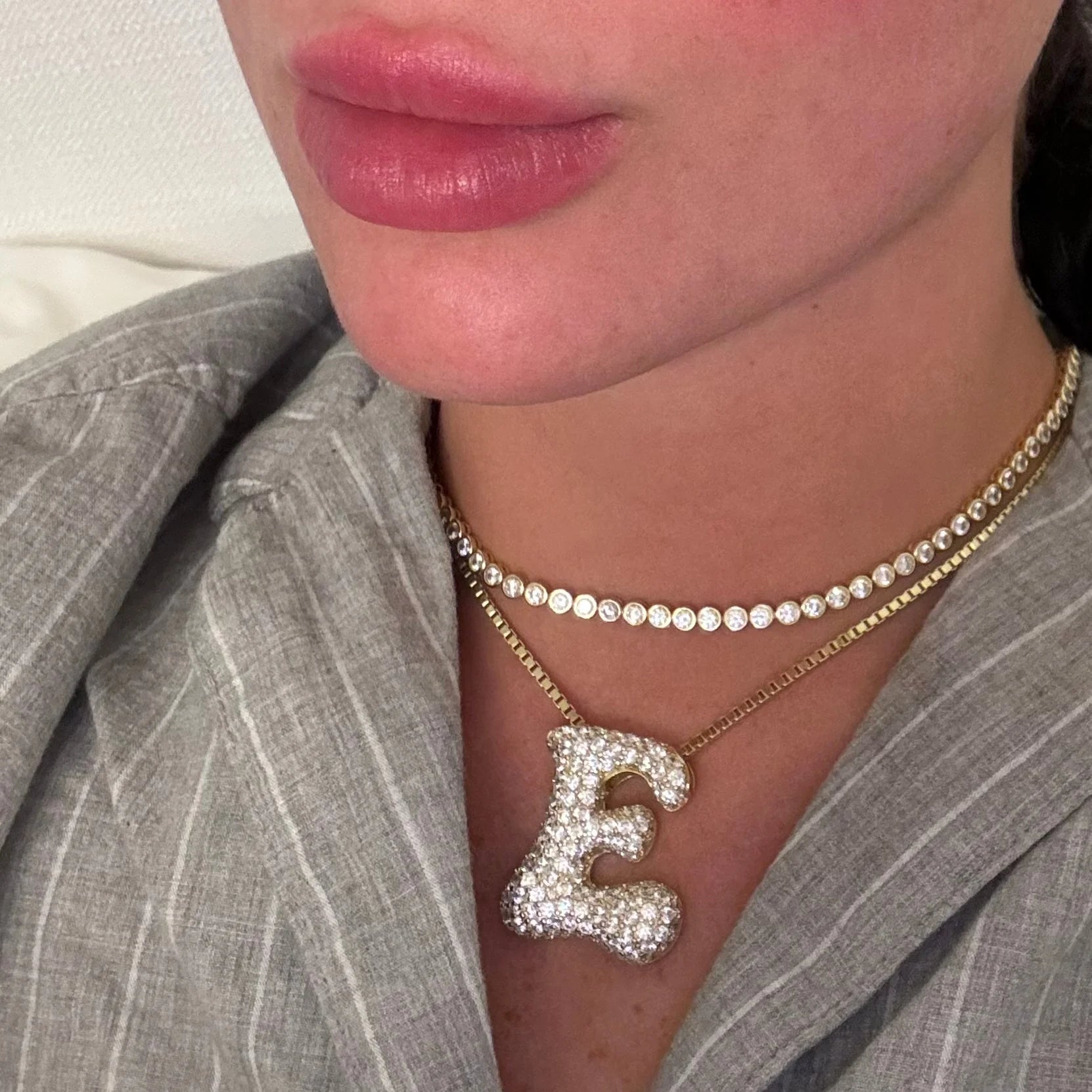 Gold iced jumbo letter E necklace layered with a tennis necklace