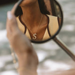 Gold iced jumbo script letter S necklace reflected in a mirror