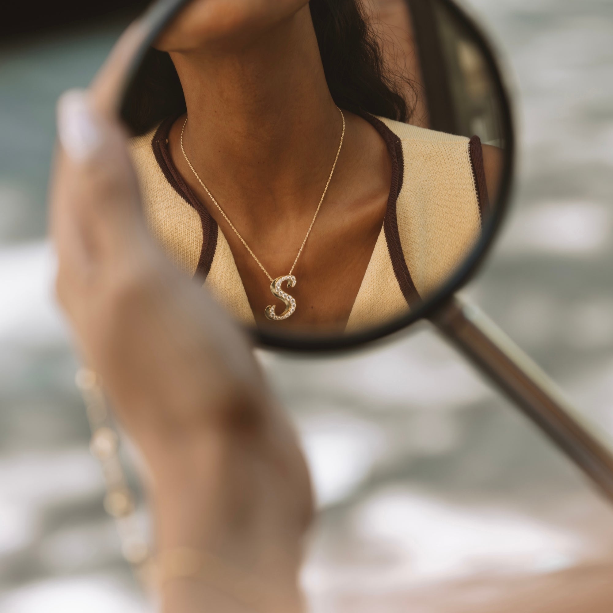 Gold iced jumbo script letter S necklace reflected in a mirror