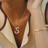 Close-up of a gold iced jumbo script letter S necklace worn with a bracelet