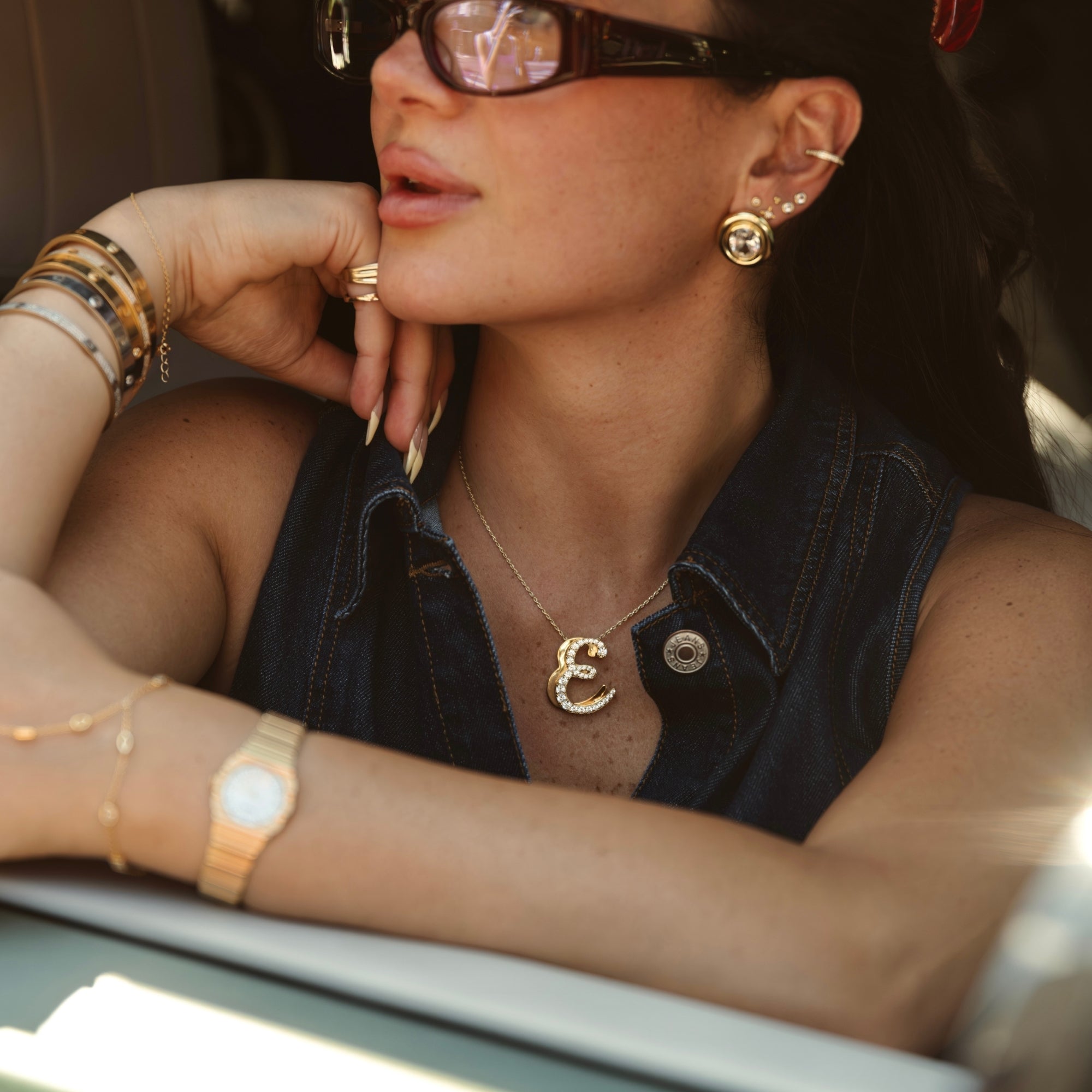 Woman in sunglasses wearing a gold iced jumbo script letter E necklace