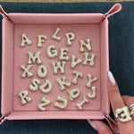 Iced medium jumbo letters scattered in a pink jewelry tray