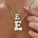 Gold iced jumbo and medium jumbo letter E necklaces held up close
