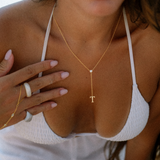 Close-up of a gold lariat letter necklace worn with a white top