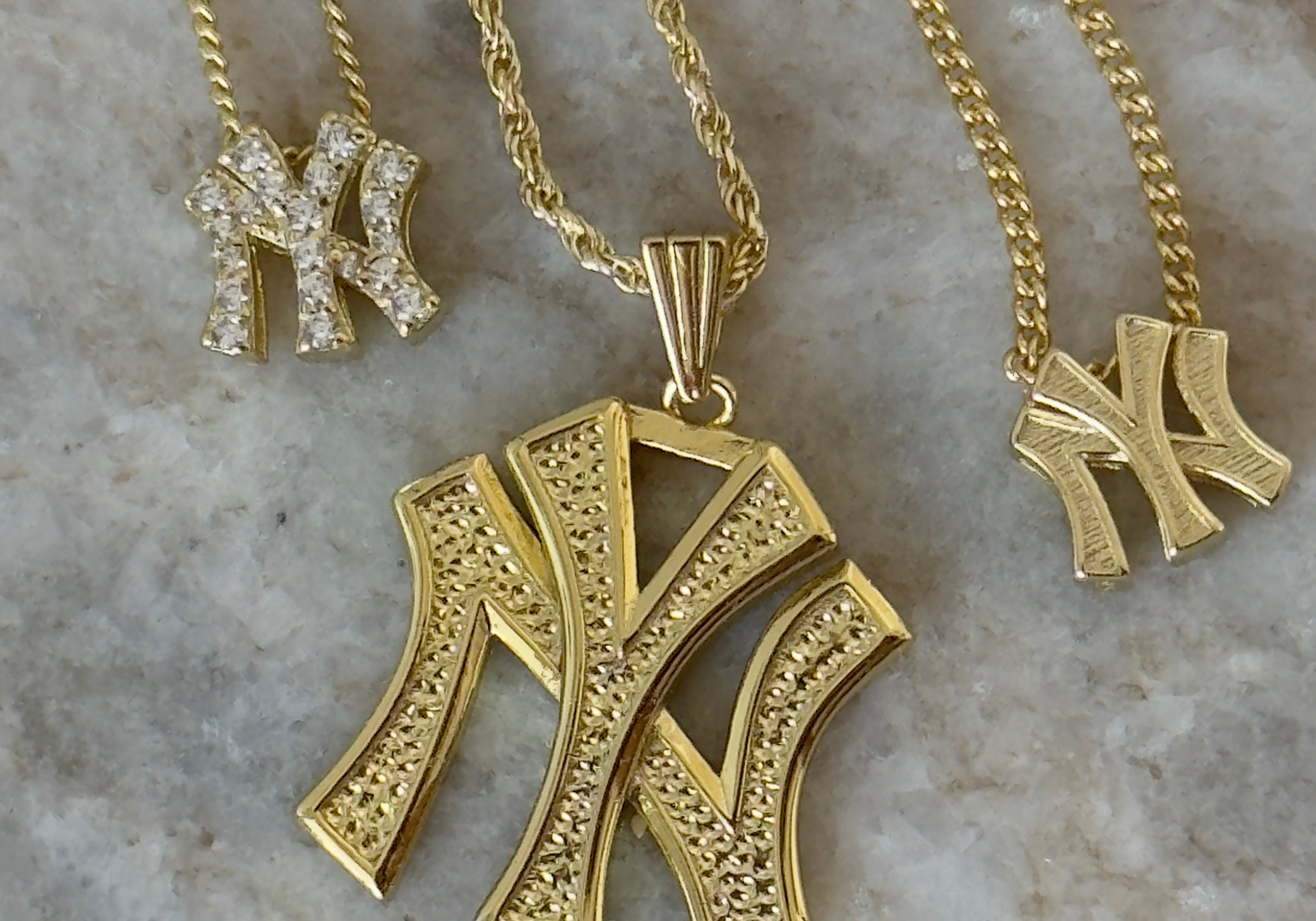 Gold NY Yankees pendants in mini, classic and CZ styles on marble