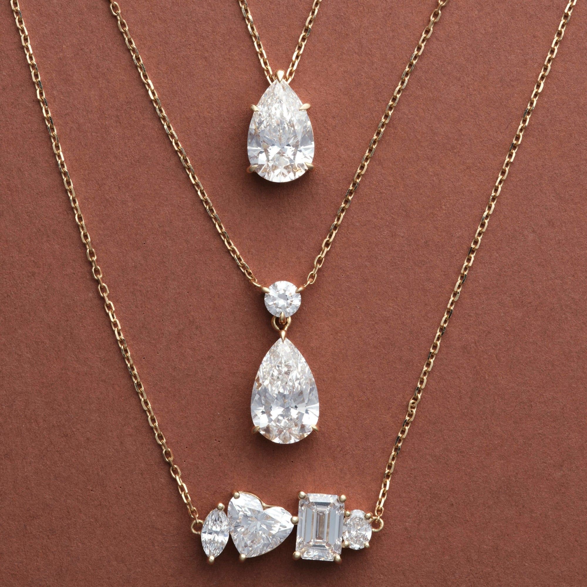 Multi Shape, Pear Dangle and Classic Pear Diamond Necklaces layered on brown, 14K solid gold