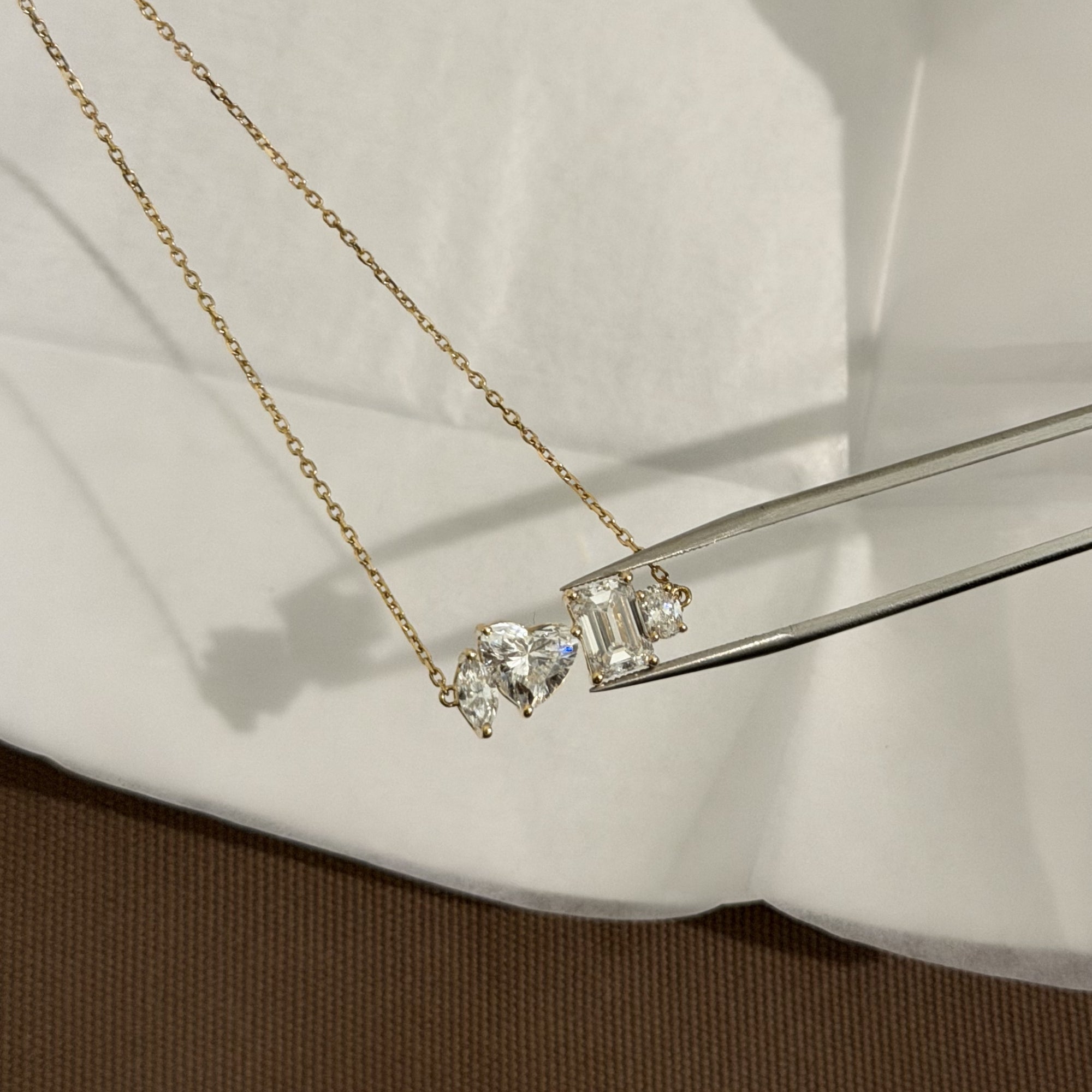 Multi Shape Diamond Necklace held with tweezers over linen, IGI Certified Lab Diamonds