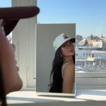 Model taking a mirror photo by a window wearing the EP Teddy Trucker Hat