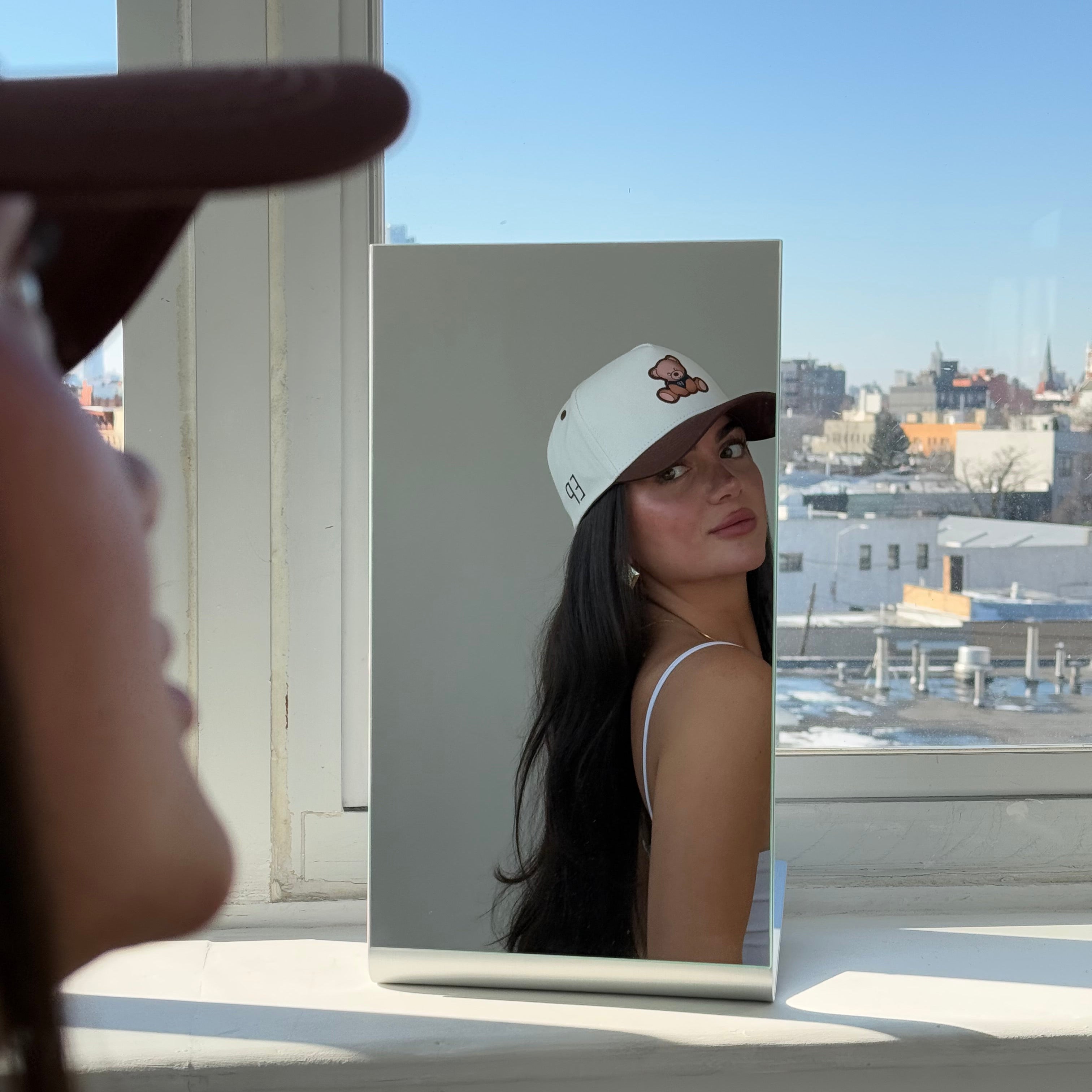 Model taking a mirror photo by a window wearing the EP Teddy Trucker Hat