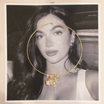 Thin gold cuff necklace with charms resting on a black and white photo print