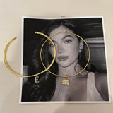 Classic and thin gold cuff necklaces with letter charms on a black and white photo