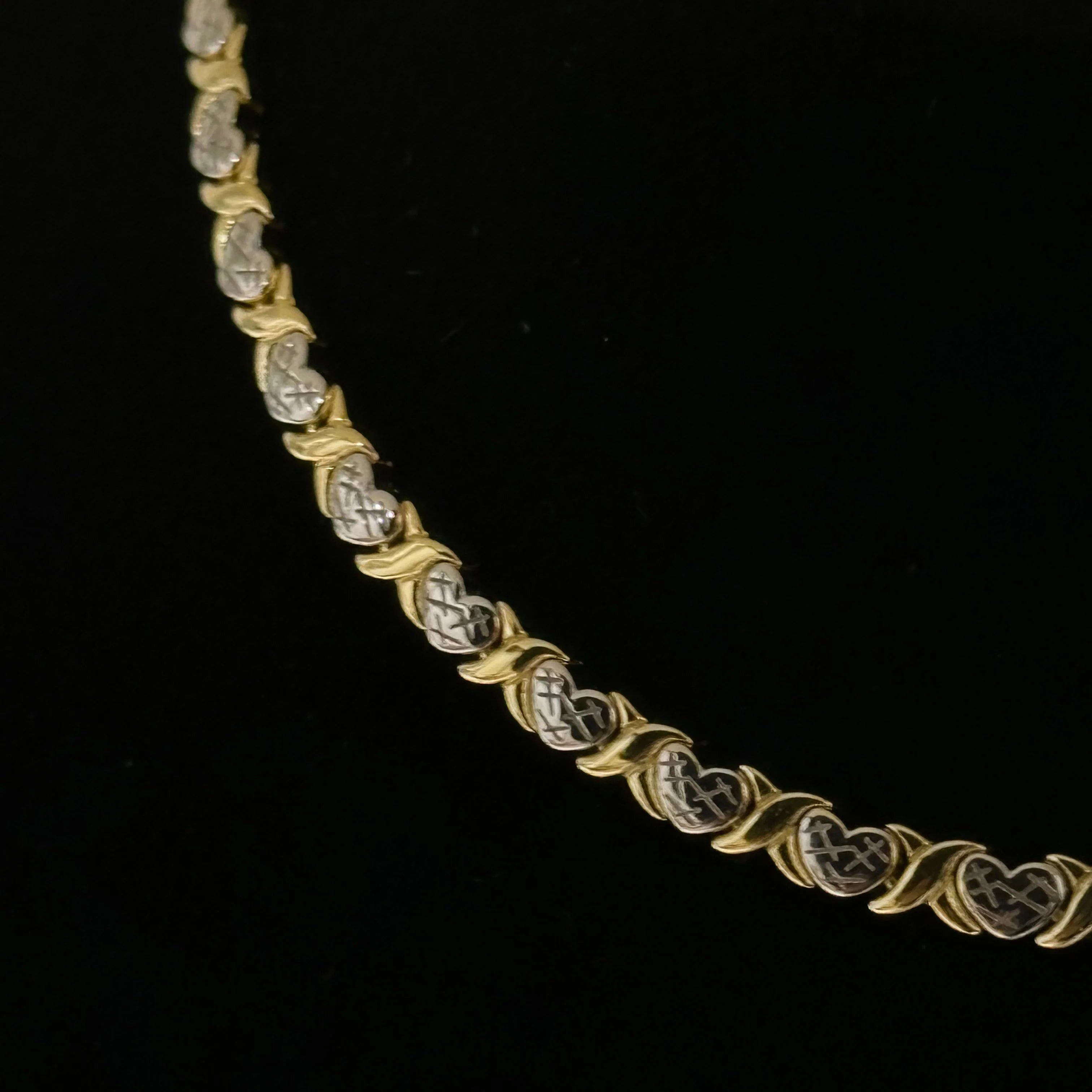 Close-up of the gold and silver XOXO Necklace on black velvet